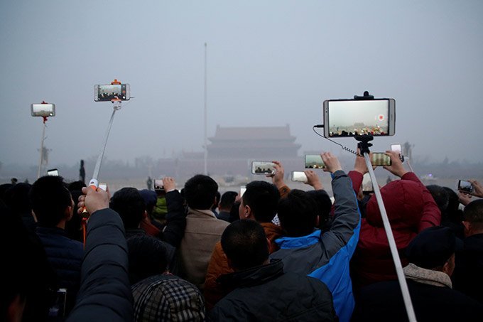 Pessoas gravam cerimônia de hasteamento de bandeira durante a poluição atmosférica na Praça Tiananmen depois que um alerta vermelho foi emitido para a poluição do ar em Pequim, China, 20 de dezembro de 2016.