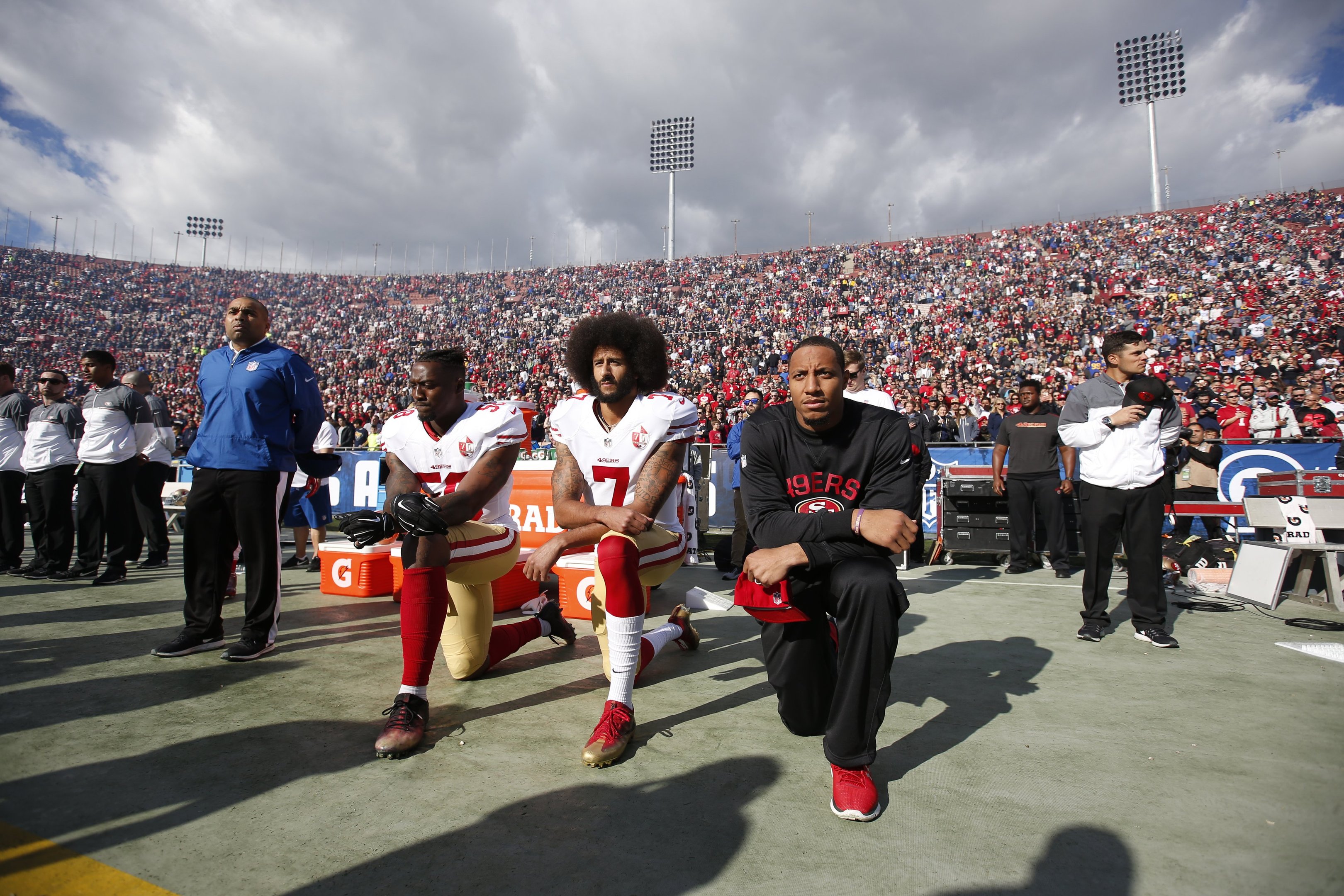 Eli Harold, Colin Kaepernick e Eric Reid do San Francisco 49ers ajoelham-se durante o hino nacional americano