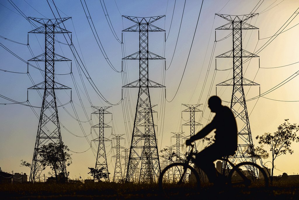 A man rides a bicycle near power lines connecting pylons of high-tension electricity, in Brasilia