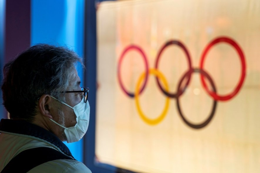 A man wearing a protective face mask, following an outbreak of the coronavirus, stands in front of The Tokyo Olympic flag 1964 at The Japan Olympics museum in Tokyo