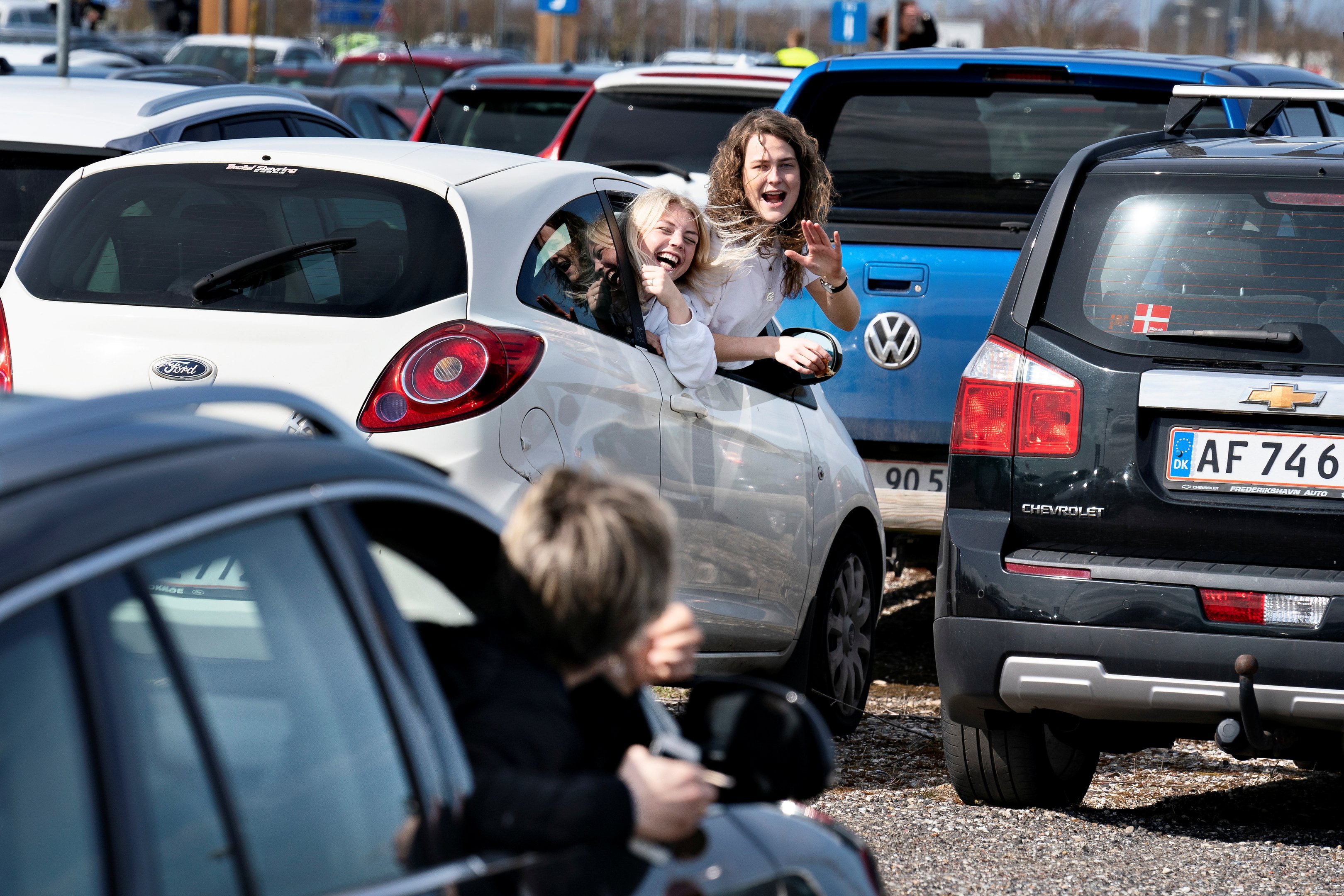 Jovens se cumprimentam de dentro de carros para serviço de Páscoa em estacionamento, na Dinamarca