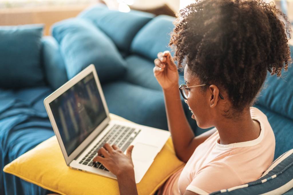 Mulher negra usando computador no sofá de casa