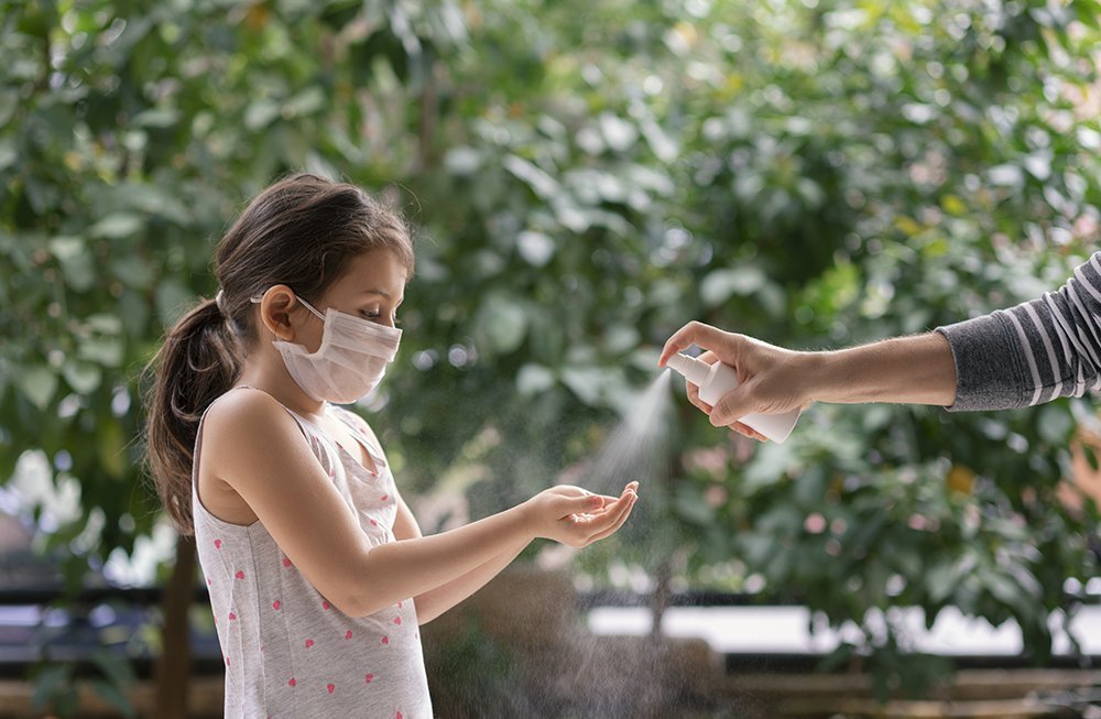 Criança de máscara passa álcool nas mãos durante a pandemia de coronavírus