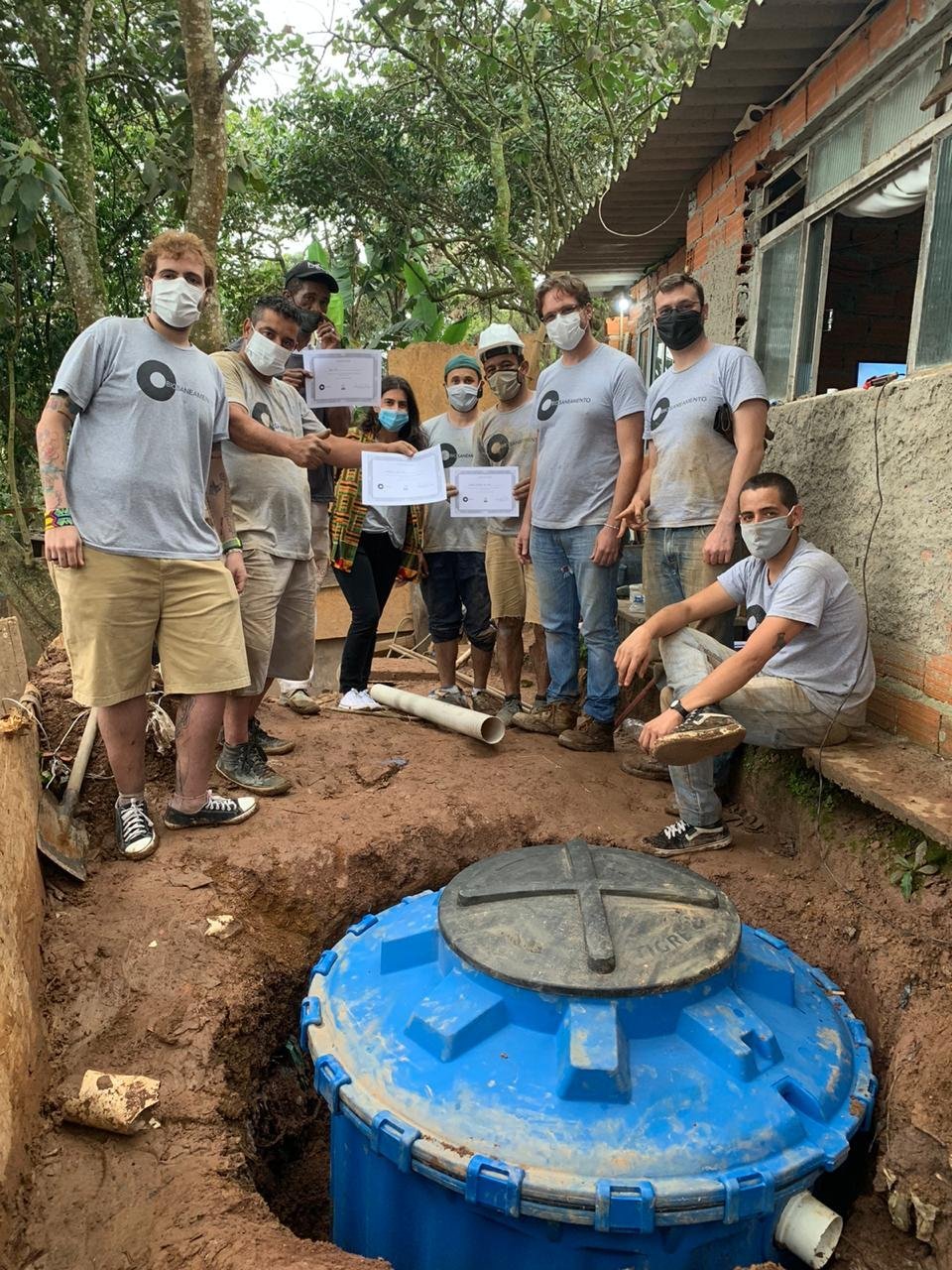 Ao lado da organizaçao da ação, moradores da comunidade Vila Moraes seguram certificado de treinamento na implantação do sistema de saneamento