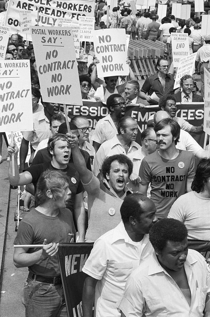 Funcionários dos correios carregando cartazes manifestam-se do lado de fora da agência pricipal, na 34th Street com a 8th Avenue, Nova York, em 20 de julho de 1978.