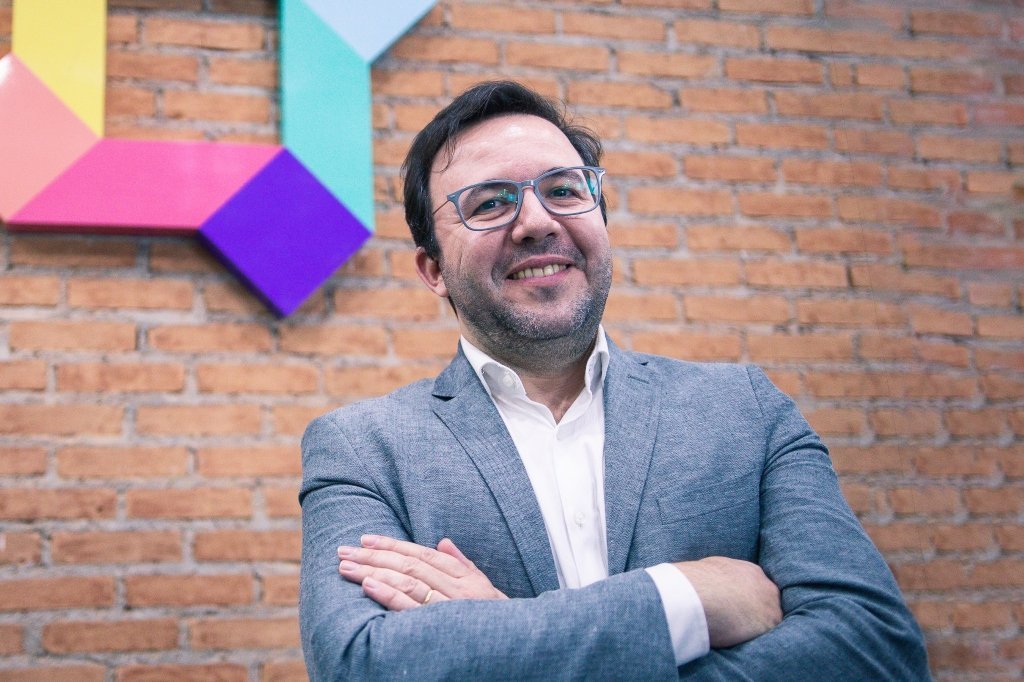 Carlos Cera, CEO da Superlogica, com os braços cruzados em frente à parede de tijolos