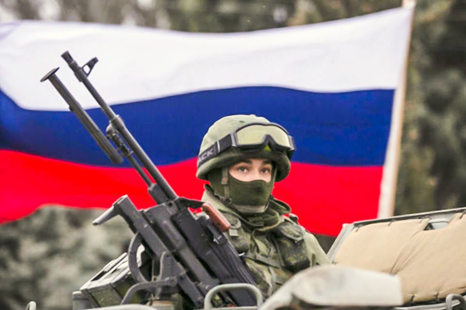 Um ativista pró-Rússia segura uma bandeira russa atrás de um militar armado no topo de um veículo do exército russo, próximo a um posto de controle de fronteira na cidade de Balaclava, na Crimeia